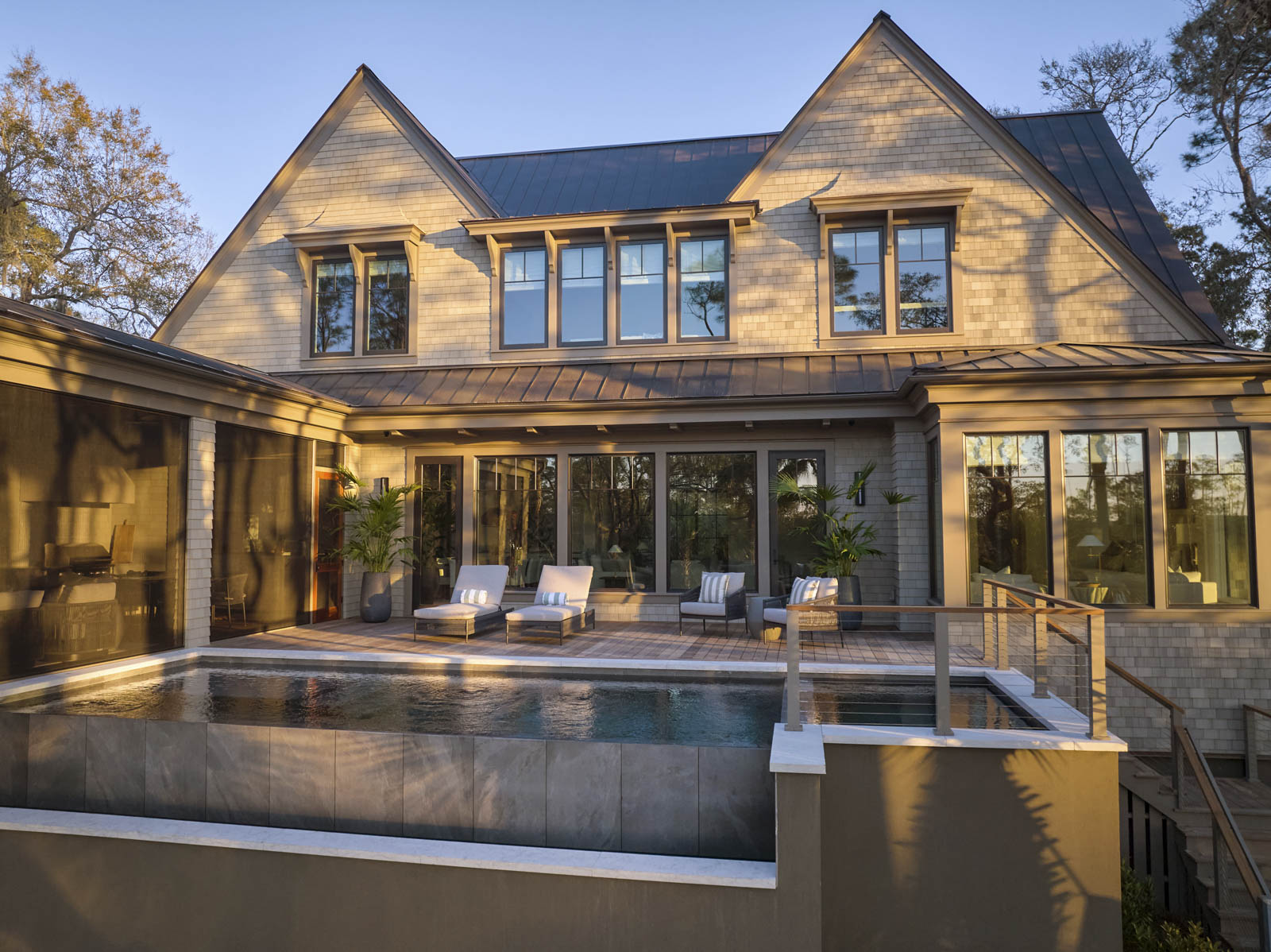 Sage-horizontal-exterior+pool-sunset Outdoor patio with television mounted to oyster shell tabby wall. White and wood patio furniture with peach-colored pillows.